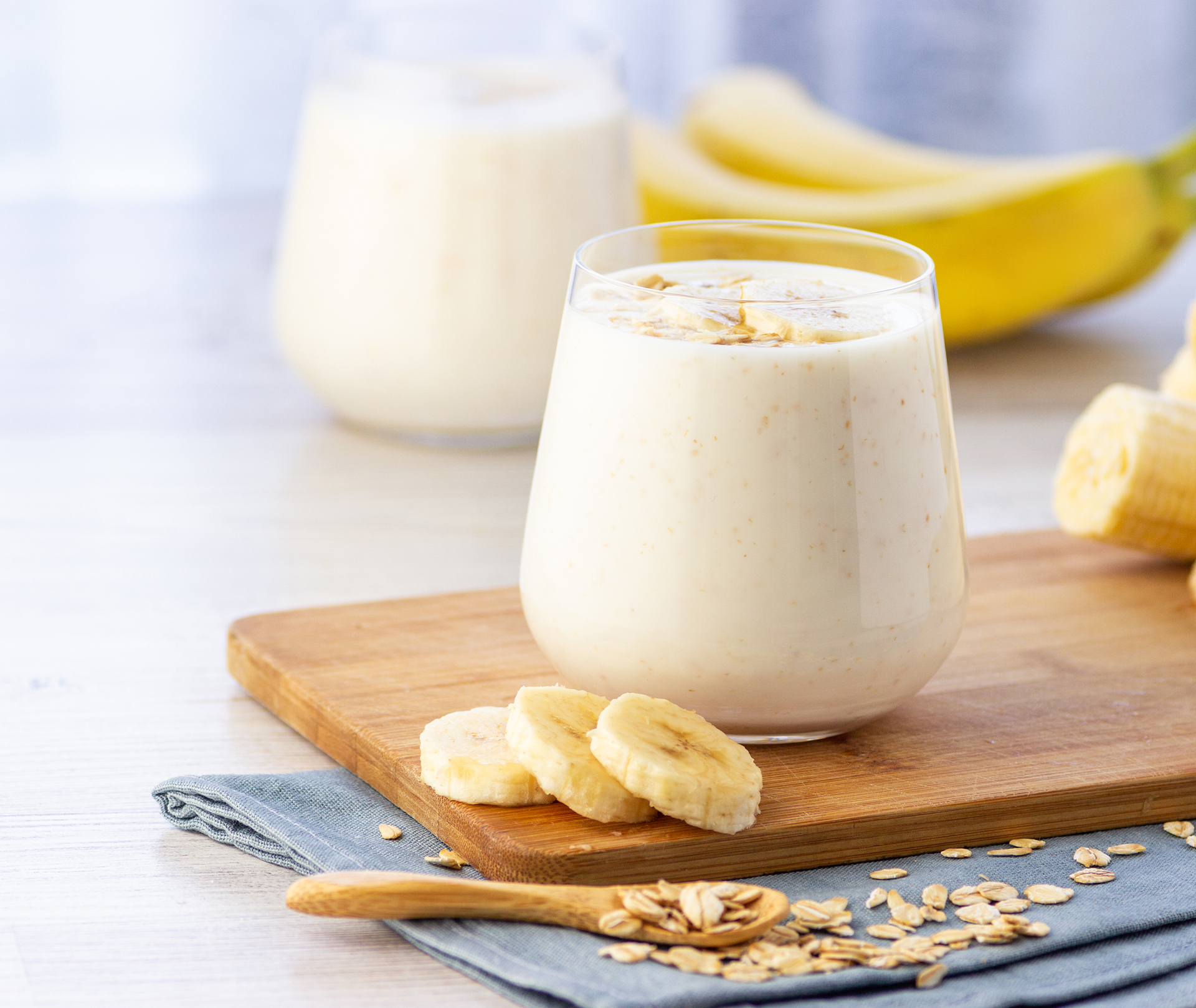 Protein-Shakes selber machen: Ganz einfach zubereiten Glas mit Proteinshake auf einem Holzbrett mit Bananenscheiben drum herum